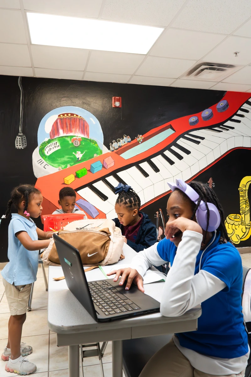 A colorful mural of a piano and performance scene adorns a classroom wall, with students engaged in various activities at tables.
