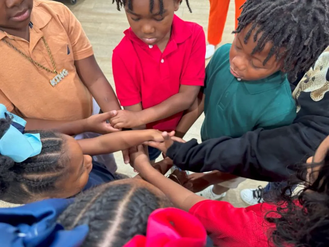 A group of kids of various ages join hands in a circle, demonstrating teamwork and friendship in a playful setting.