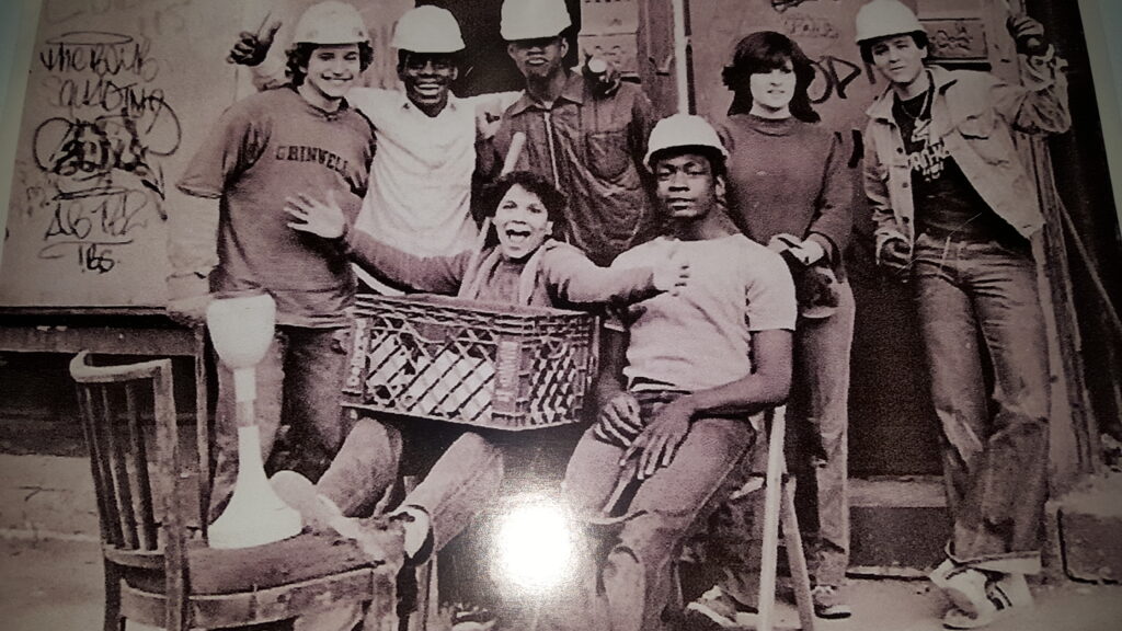 <br />Students participate in an educational activity using laptops, while an adult facilitator stands at a podium displaying the "Quality Life Center" logo in the background.