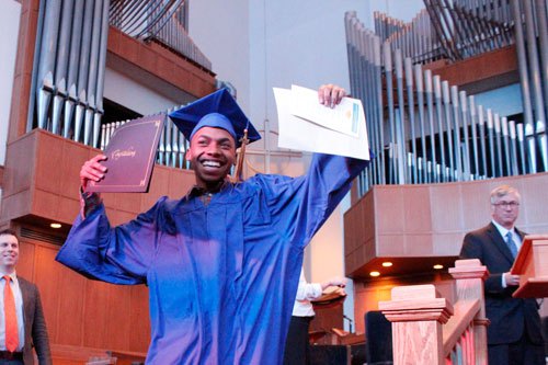 Close-up view of a person painting a large, pink cartoon face with a wide smile onto paper, surrounded by other people painting rocks and using acrylic paints.
